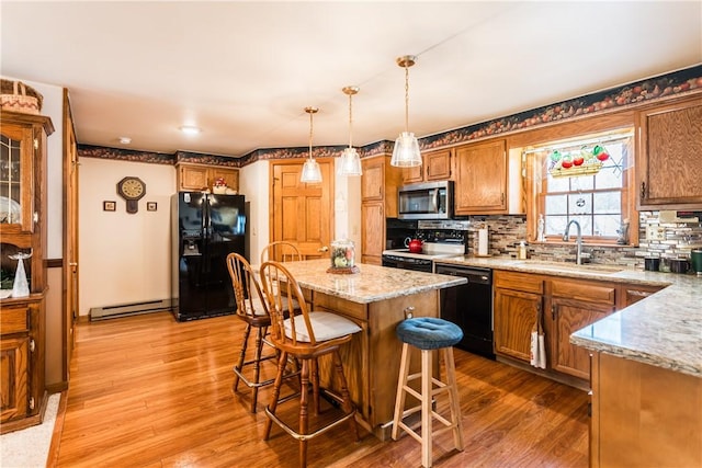 kitchen with light hardwood / wood-style flooring, pendant lighting, sink, a center island, and black appliances