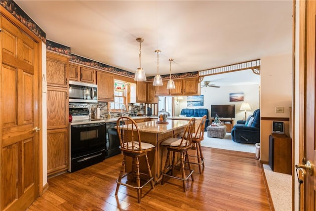 kitchen with electric range oven, light stone countertops, a kitchen island, decorative light fixtures, and a breakfast bar area