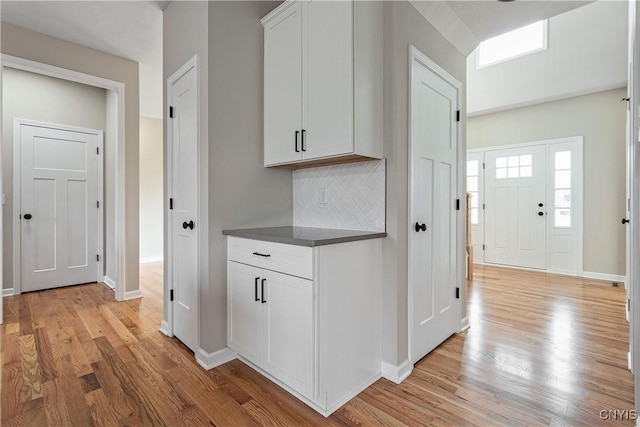 kitchen with decorative backsplash, white cabinetry, and light wood-type flooring