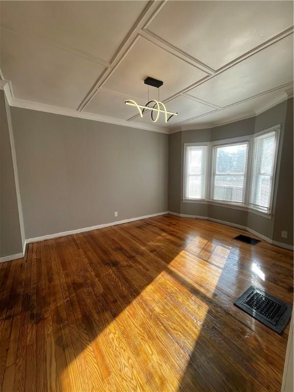 spare room with coffered ceiling, ornamental molding, an inviting chandelier, and wood-type flooring