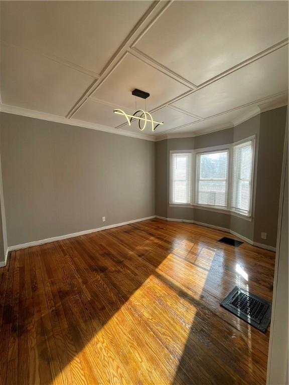 empty room featuring hardwood / wood-style floors, coffered ceiling, a notable chandelier, and ornamental molding