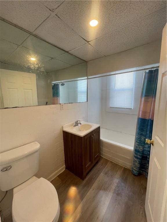 full bathroom featuring toilet, hardwood / wood-style floors, shower / bath combo with shower curtain, a drop ceiling, and vanity