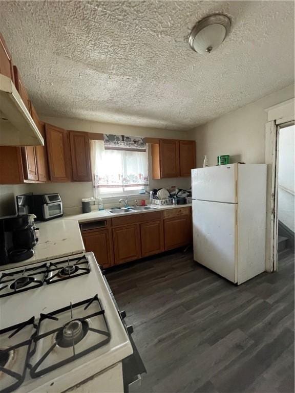 kitchen with sink, white appliances, a textured ceiling, and dark wood-type flooring