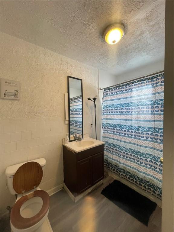 bathroom with toilet, a textured ceiling, wood-type flooring, vanity, and a shower with curtain