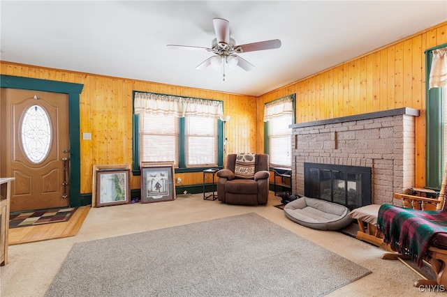 carpeted living room with a brick fireplace, wooden walls, ceiling fan, and a healthy amount of sunlight