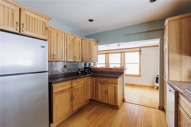 kitchen featuring backsplash, heating unit, dark stone countertops, light hardwood / wood-style floors, and stainless steel appliances