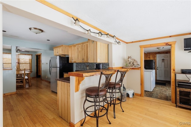 kitchen with light brown cabinets, tasteful backsplash, kitchen peninsula, crown molding, and a breakfast bar area