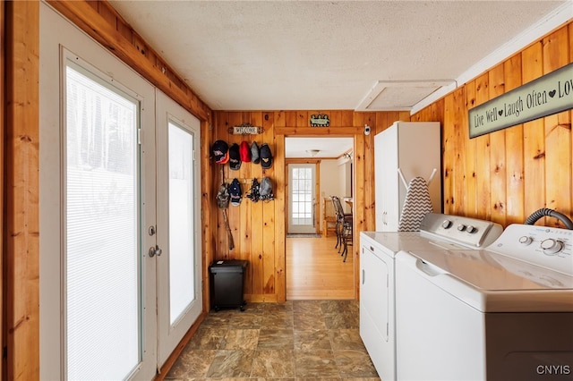 clothes washing area with washer and dryer, a textured ceiling, french doors, and wooden walls