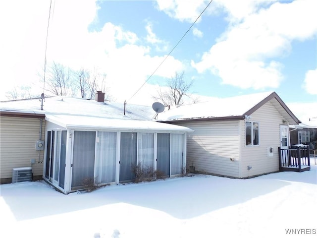 snow covered rear of property featuring central AC unit and a sunroom