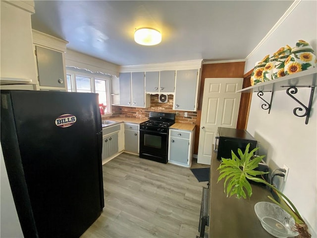 kitchen featuring crown molding, light wood-type flooring, white cabinets, black appliances, and decorative backsplash