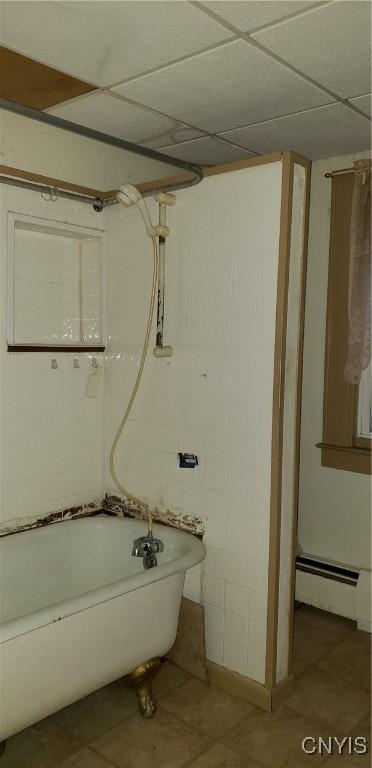 bathroom with a drop ceiling, tile patterned floors, a baseboard heating unit, and washtub / shower combination