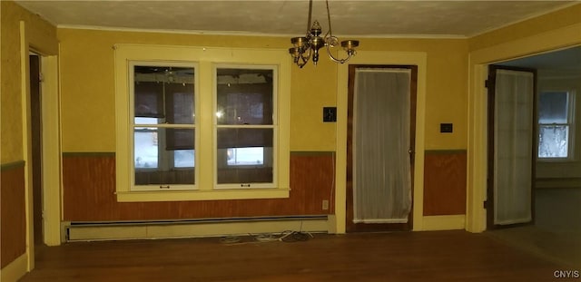 unfurnished room with crown molding, a chandelier, a baseboard heating unit, dark wood-type flooring, and wood walls