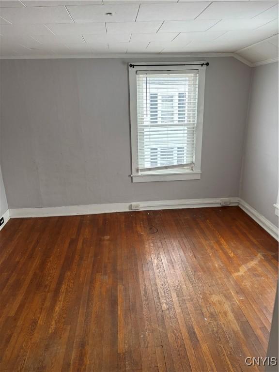 spare room featuring dark wood-type flooring, lofted ceiling, and ornamental molding