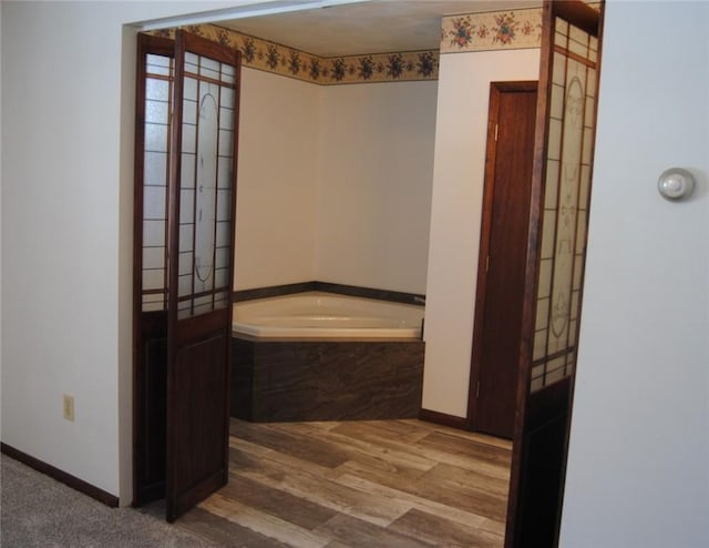 bathroom with a relaxing tiled tub and wood-type flooring