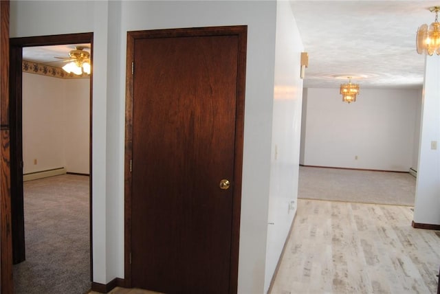 hallway featuring a textured ceiling, baseboard heating, a chandelier, and light colored carpet