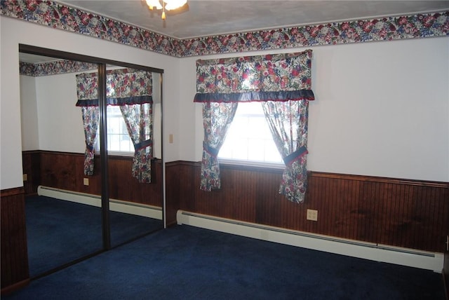 unfurnished room with a baseboard radiator, wooden walls, and carpet flooring