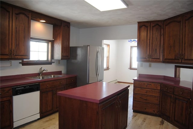 kitchen featuring dishwasher, a kitchen island, sink, stainless steel refrigerator, and light hardwood / wood-style flooring