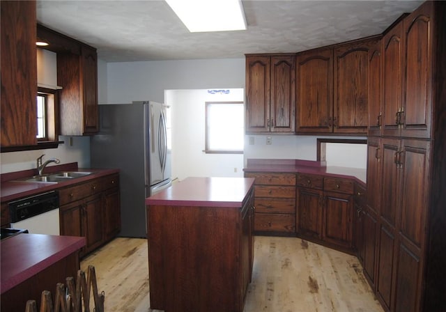 kitchen with white dishwasher, stainless steel refrigerator, sink, a kitchen island, and light hardwood / wood-style flooring