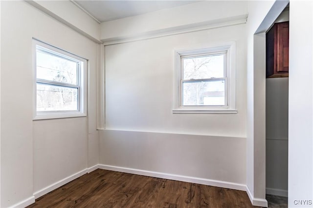 empty room with a wealth of natural light and dark hardwood / wood-style flooring