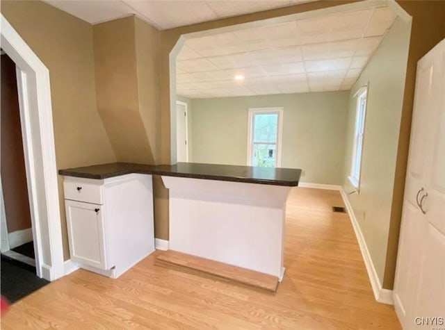 kitchen with light hardwood / wood-style flooring, white cabinetry, kitchen peninsula, and a drop ceiling