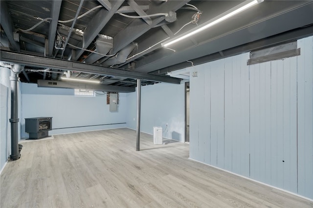 basement featuring hardwood / wood-style floors, electric panel, and a wood stove