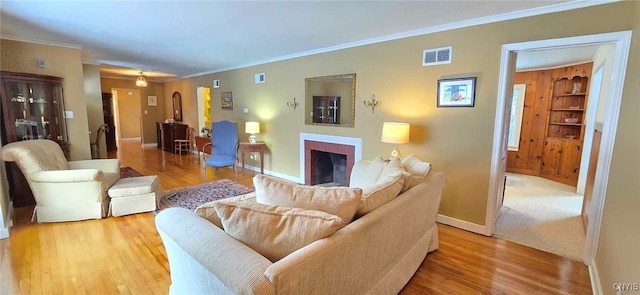 living room featuring built in shelves, light hardwood / wood-style flooring, and crown molding