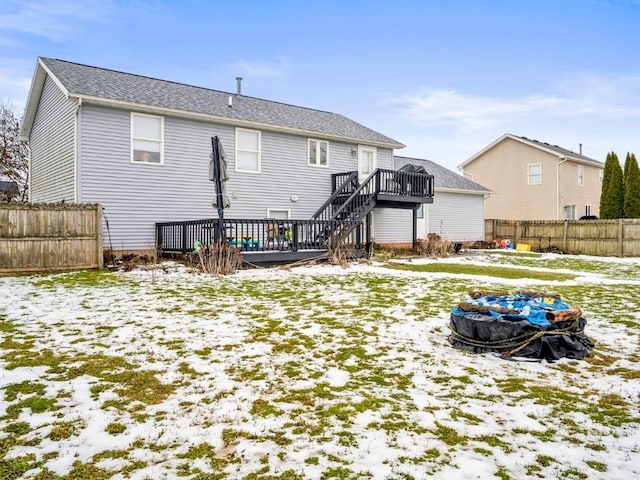 snow covered rear of property with a wooden deck and a fire pit