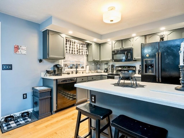 kitchen featuring black appliances, gray cabinetry, a kitchen breakfast bar, light wood-type flooring, and sink