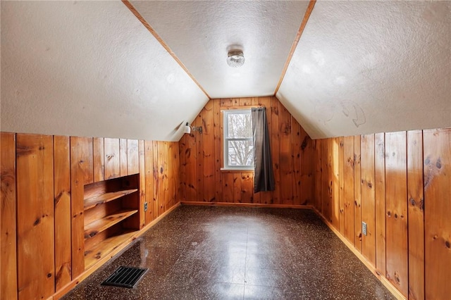 bonus room featuring a textured ceiling, wood walls, and vaulted ceiling