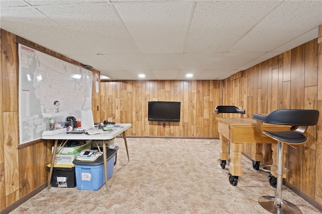 recreation room featuring light colored carpet, a paneled ceiling, and wood walls