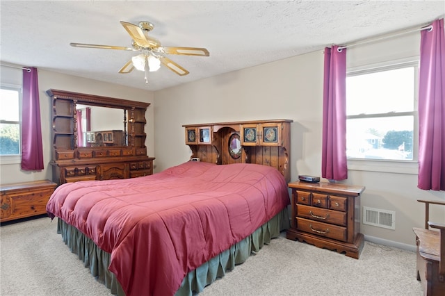 bedroom with light carpet, multiple windows, a textured ceiling, and ceiling fan