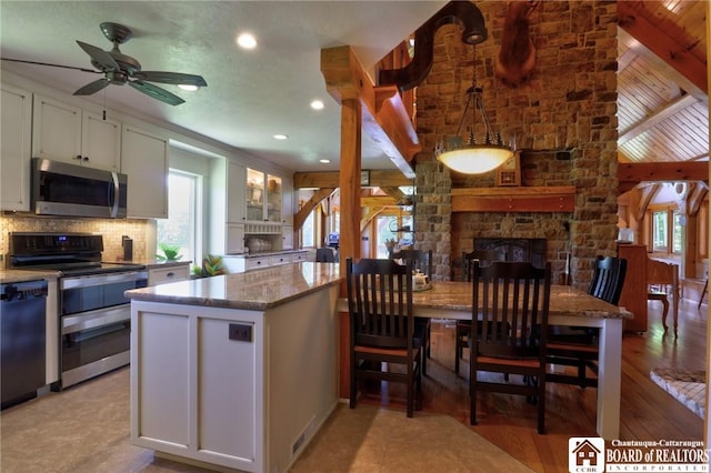 kitchen with light stone countertops, appliances with stainless steel finishes, white cabinets, a kitchen island, and ceiling fan