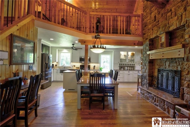 dining space with a towering ceiling, a stone fireplace, wood walls, and hardwood / wood-style flooring