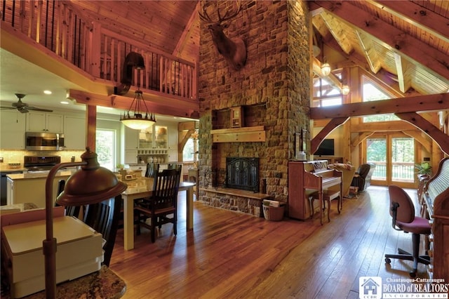 interior space featuring a stone fireplace, wood ceiling, hardwood / wood-style flooring, high vaulted ceiling, and ceiling fan