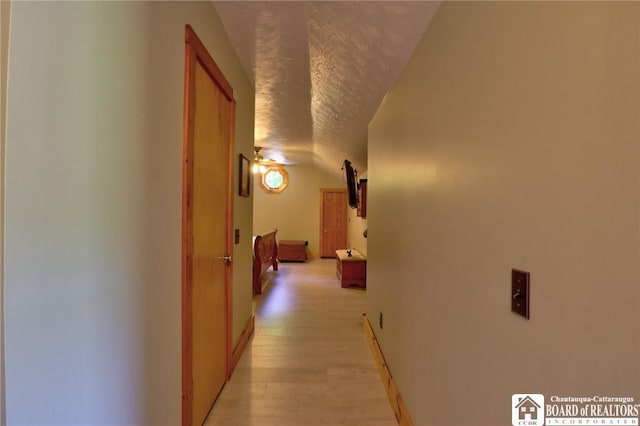 hallway with vaulted ceiling, light hardwood / wood-style floors, and a textured ceiling