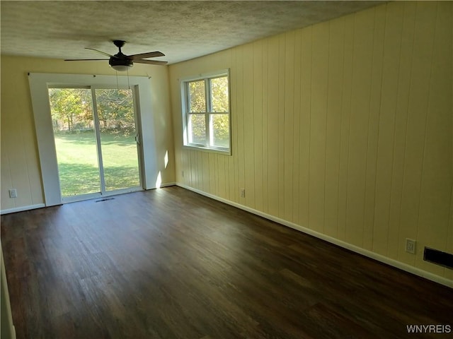 unfurnished room with wood walls, dark wood-type flooring, and a wealth of natural light