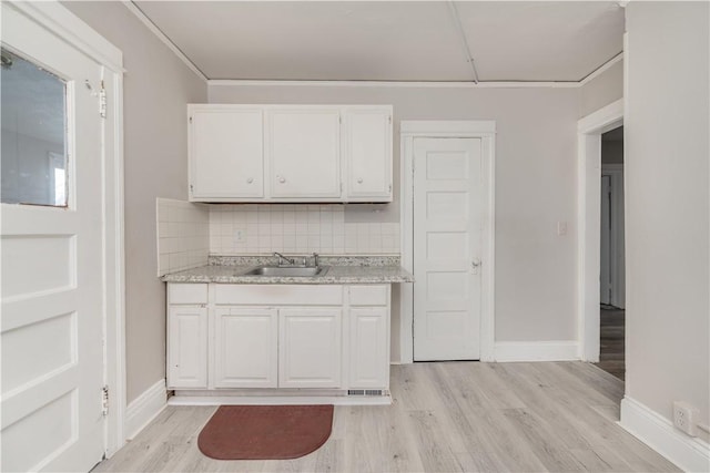 kitchen with sink, light wood-type flooring, white cabinets, and decorative backsplash