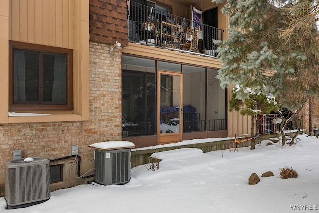 snow covered rear of property featuring central AC