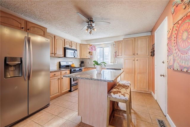 kitchen with a kitchen island, a kitchen bar, light tile patterned floors, stainless steel appliances, and a textured ceiling