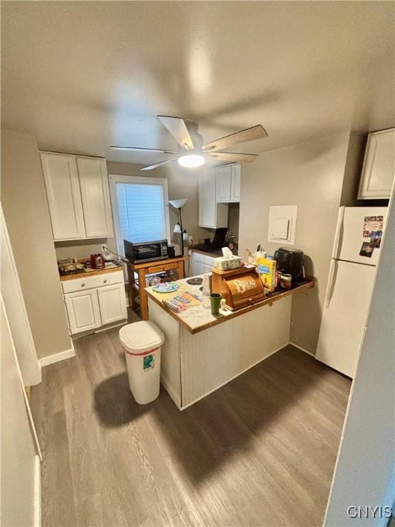 kitchen featuring hardwood / wood-style flooring, white cabinetry, white refrigerator, and kitchen peninsula