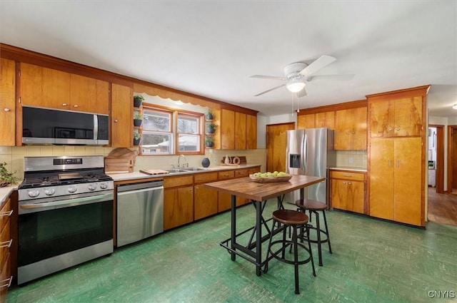 kitchen featuring ceiling fan, tasteful backsplash, sink, stainless steel appliances, and a breakfast bar area