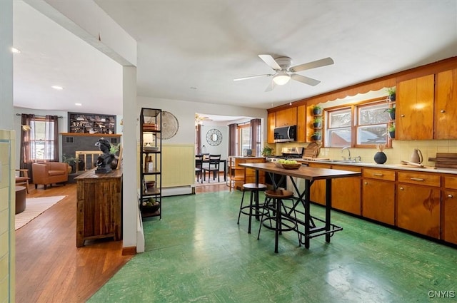 kitchen featuring baseboard heating, ceiling fan, sink, stove, and a breakfast bar area