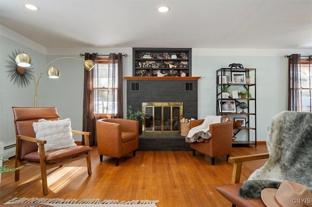 sitting room featuring a brick fireplace, wood-type flooring, and a baseboard heating unit