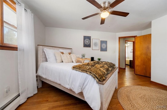 bedroom with ceiling fan, a baseboard heating unit, and light wood-type flooring