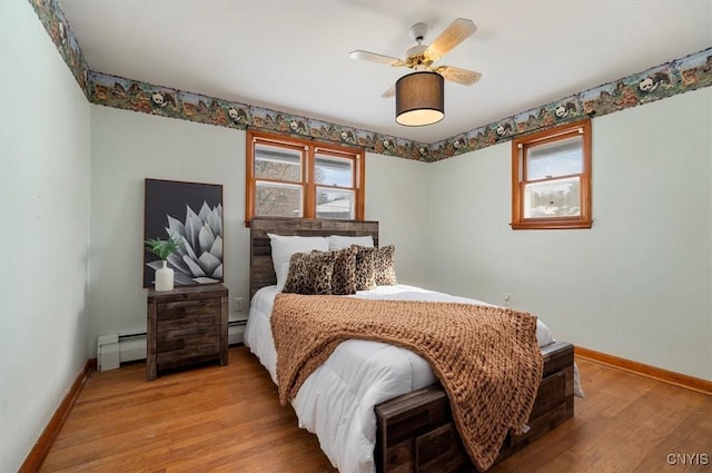 bedroom featuring ceiling fan, baseboard heating, multiple windows, and light hardwood / wood-style floors