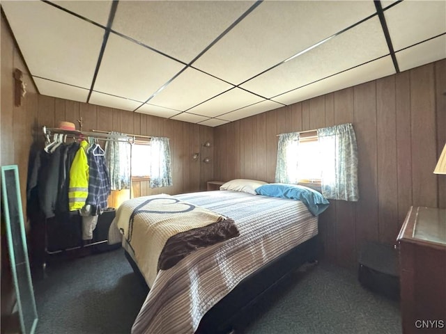 bedroom with wood walls, a drop ceiling, multiple windows, and dark colored carpet