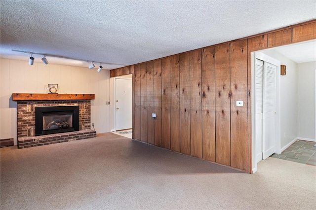 unfurnished living room featuring a fireplace, a textured ceiling, wooden walls, track lighting, and carpet