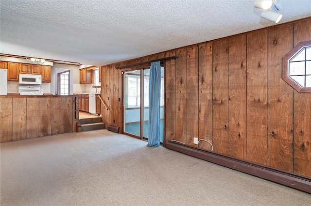 unfurnished living room featuring light colored carpet, baseboard heating, a textured ceiling, and wooden walls