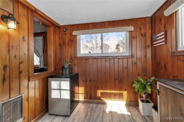 doorway to outside featuring a textured ceiling, light hardwood / wood-style flooring, and wood walls