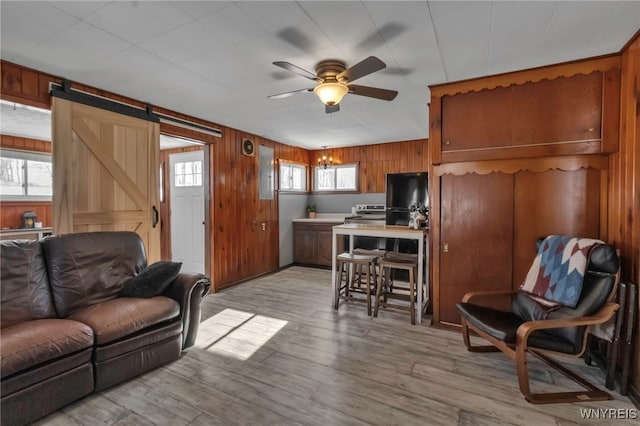 living room featuring ceiling fan, plenty of natural light, light hardwood / wood-style flooring, and wooden walls